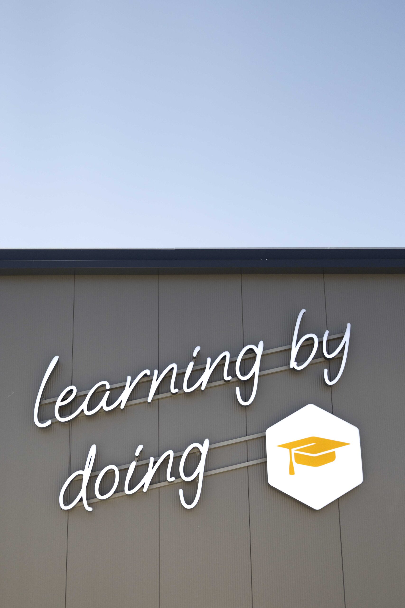 Leuchtschriftzug „Learning by doing“ mit Akademie-Symbol an der Fassade der Campingwelt Baden